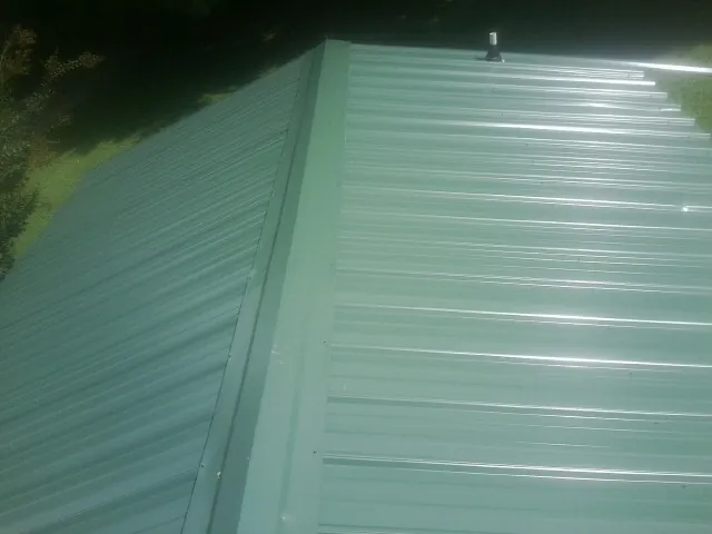 New green metal panels meeting at the ridge of a roof — Flat Roof Repair work by our crew in Troy